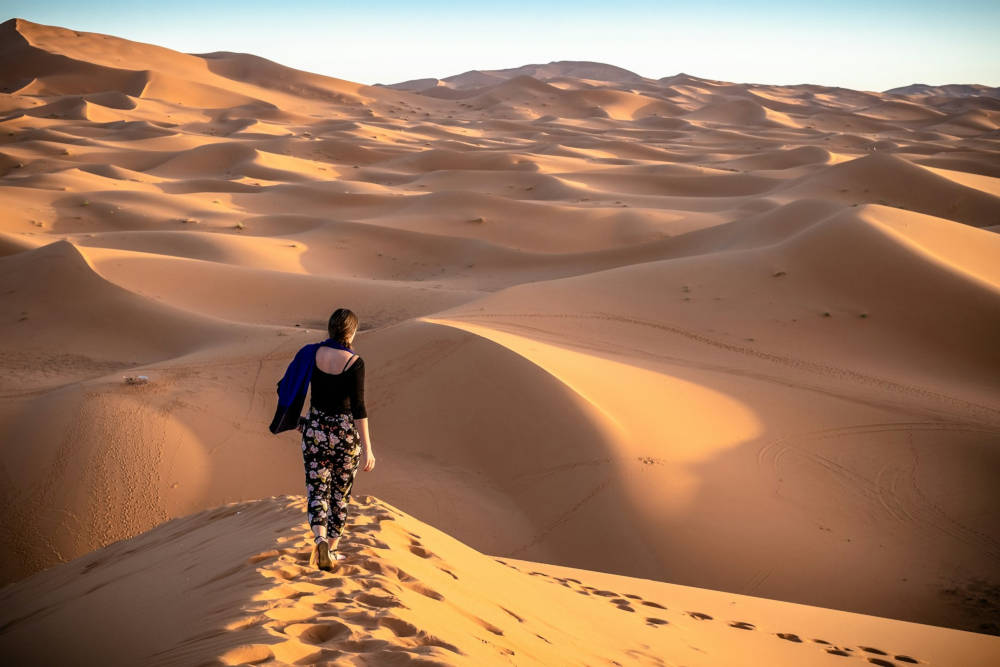 a young woman walking on the edge of a dune in an open desert